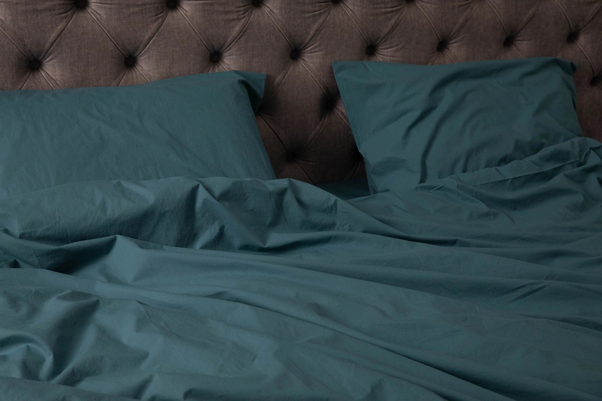 Supreme Rest’s deep teal bedding set styled against a tufted headboard, highlighting custom made elegance and eco-friendly materials for refined comfort