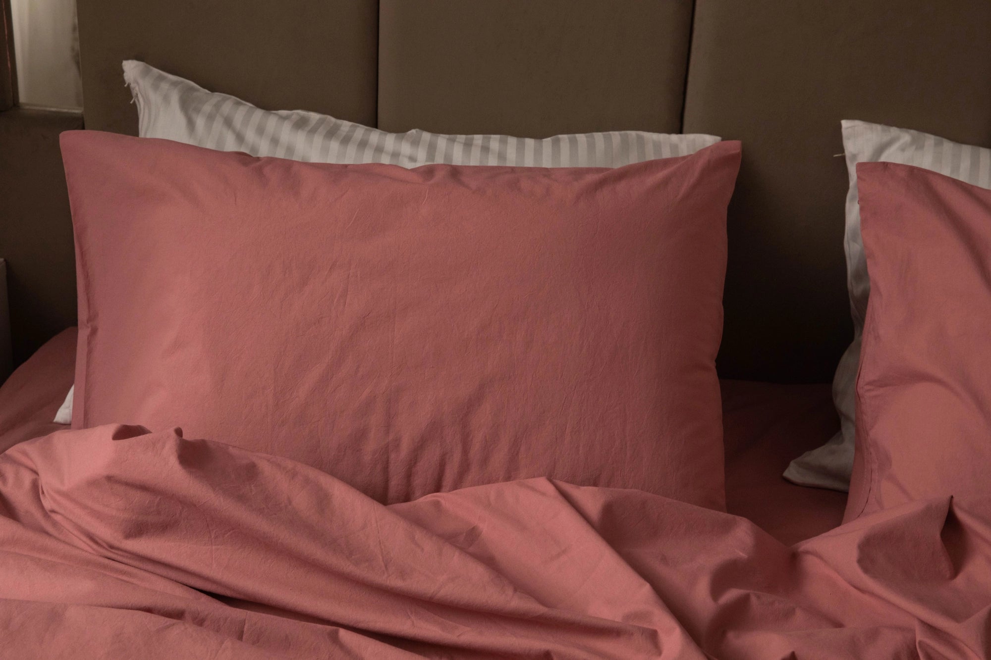 Supreme Rest rose-toned pillowcases layered over striped cotton shams—custom made for luxurious comfort with an eco-friendly, crafted aesthetic