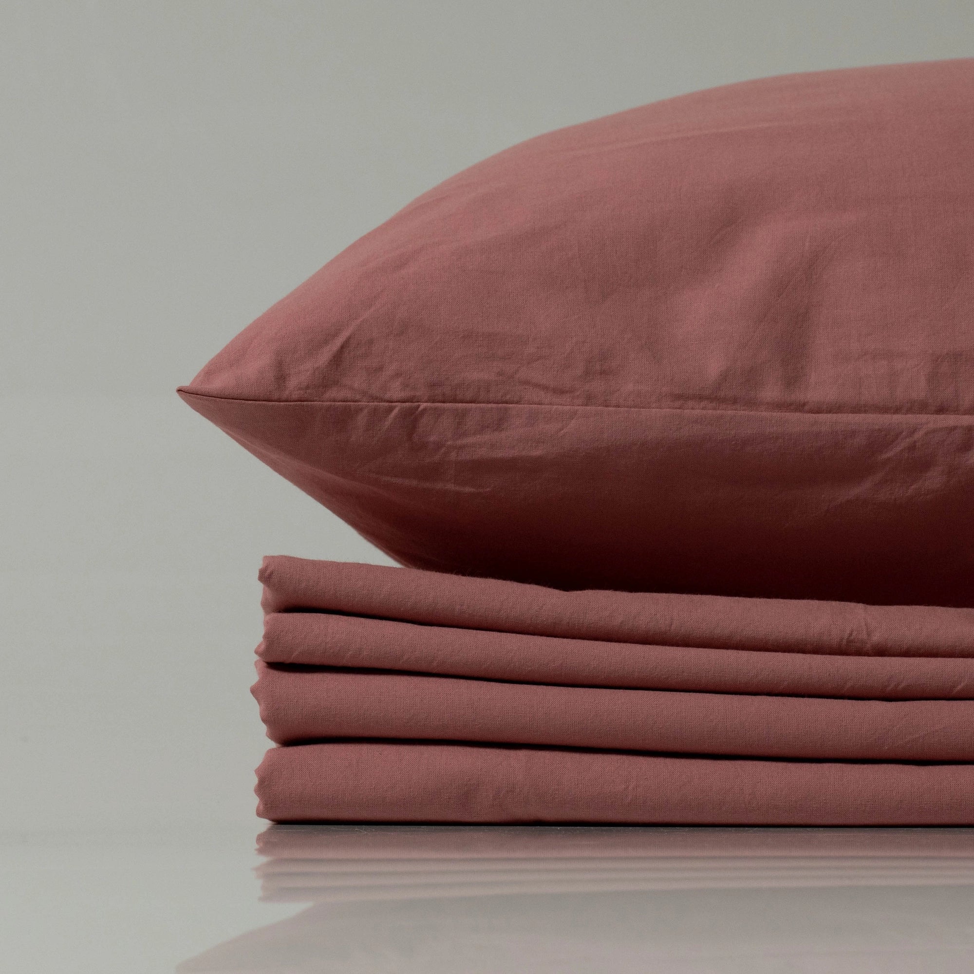 Supreme Rest stonewashed cotton sheet set in a muted rose shade, featuring a folded flat sheet and matching pillowcase—crafted for relaxed elegance and eco-friendly comfort