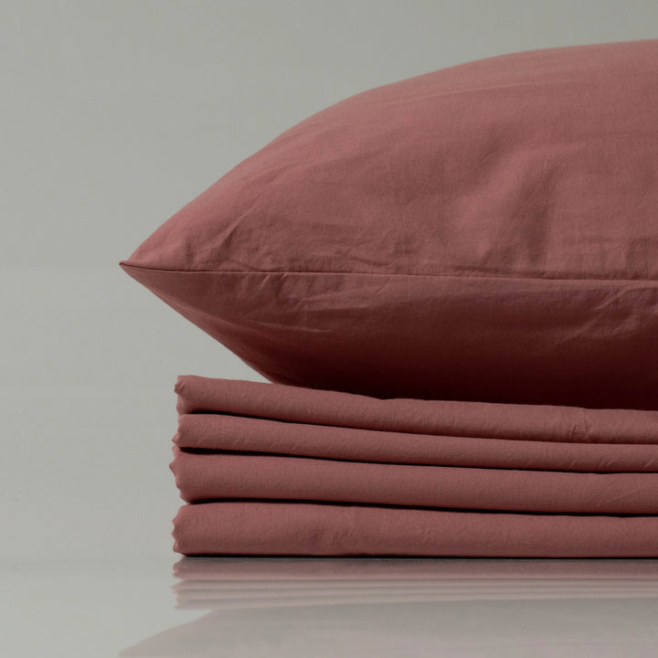 Supreme Rest stonewashed cotton sheet set in a muted rose shade, featuring a folded flat sheet and matching pillowcase—crafted for relaxed elegance and eco-friendly comfort