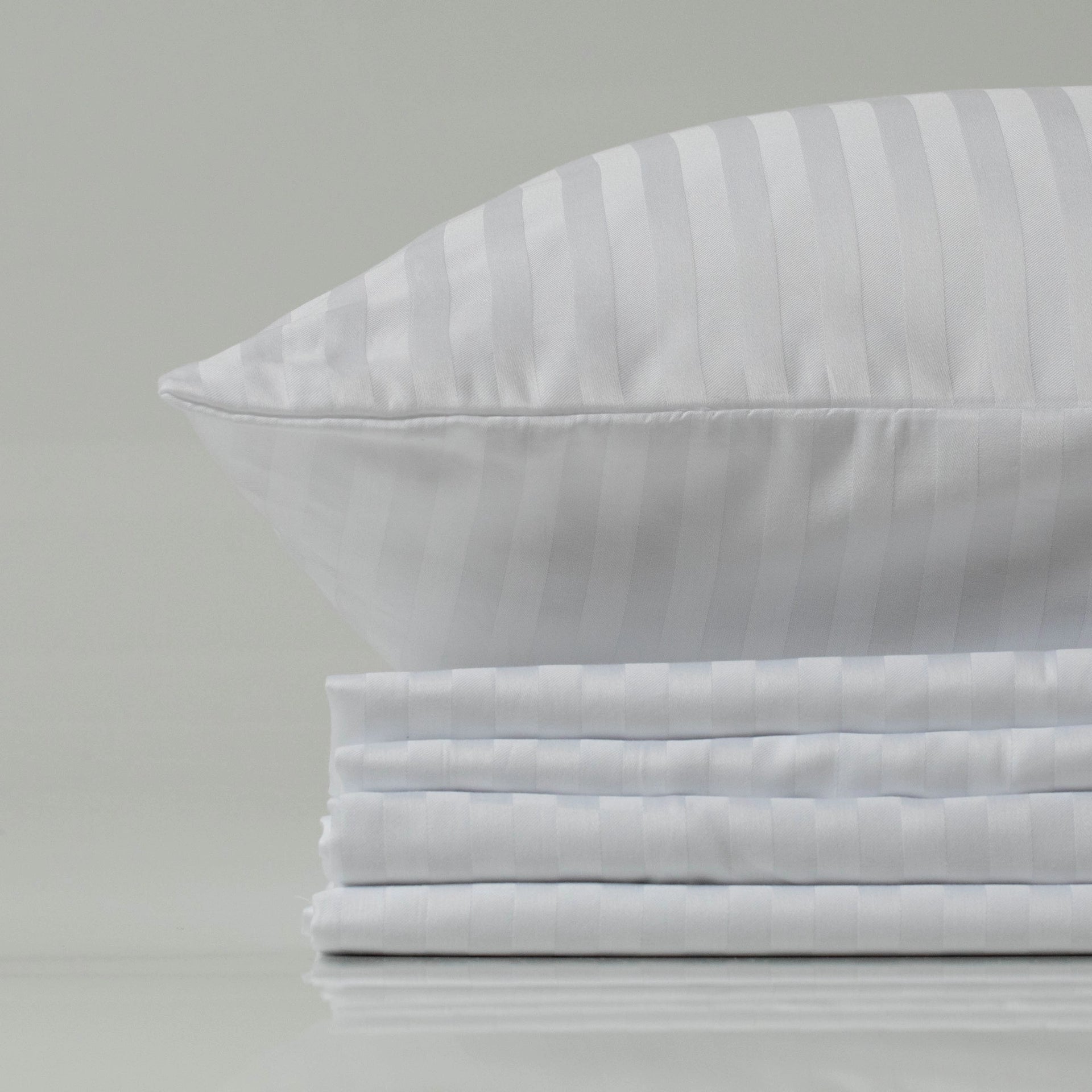 Stack of crisp, folded white sateen-striped bed sheets topped with a matching pillow, conveying a clean, polished hotel-style luxury