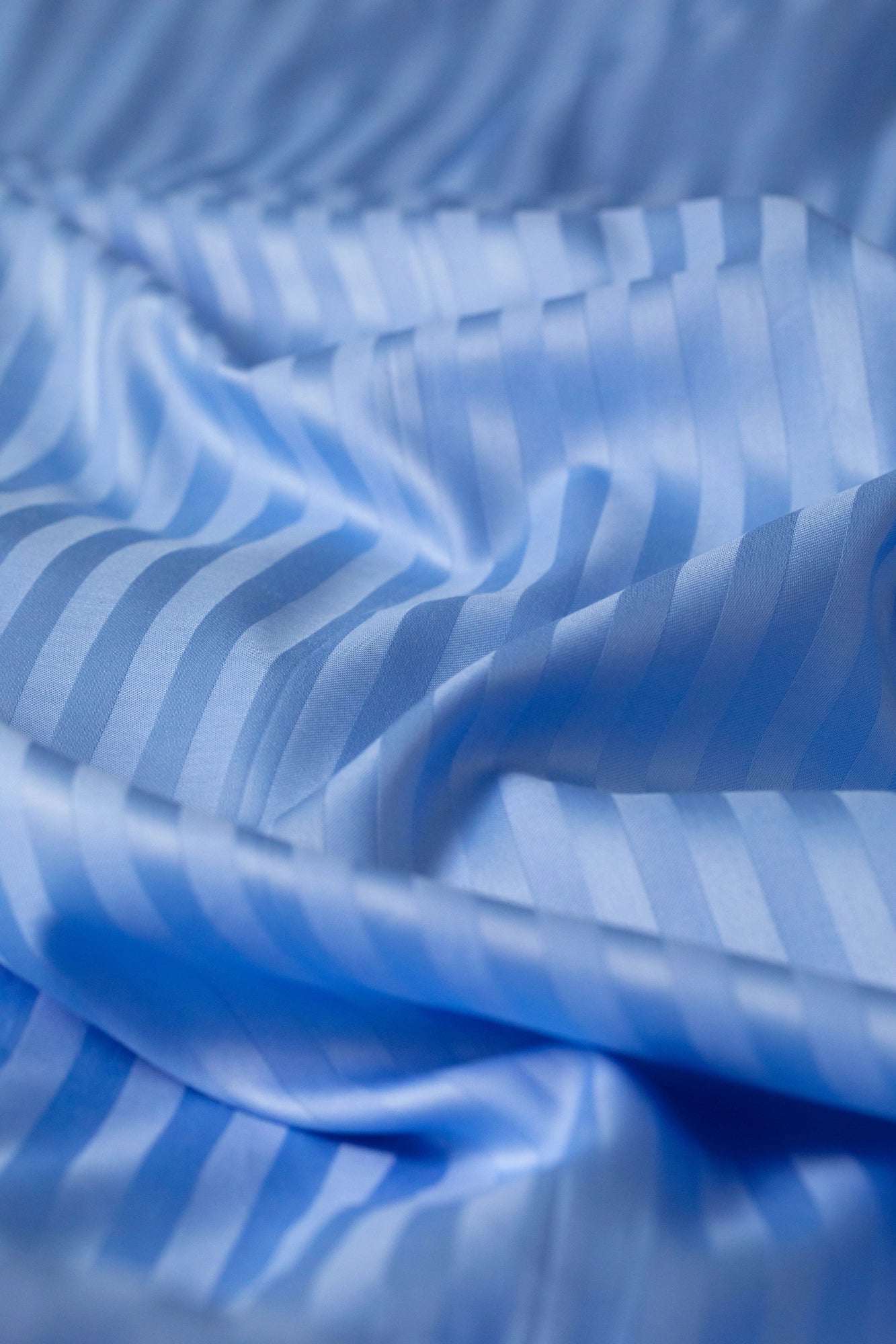Close-up of Supreme Rest Celestial Blue striped sateen fabric, showcasing its silky texture and elegant sheen.