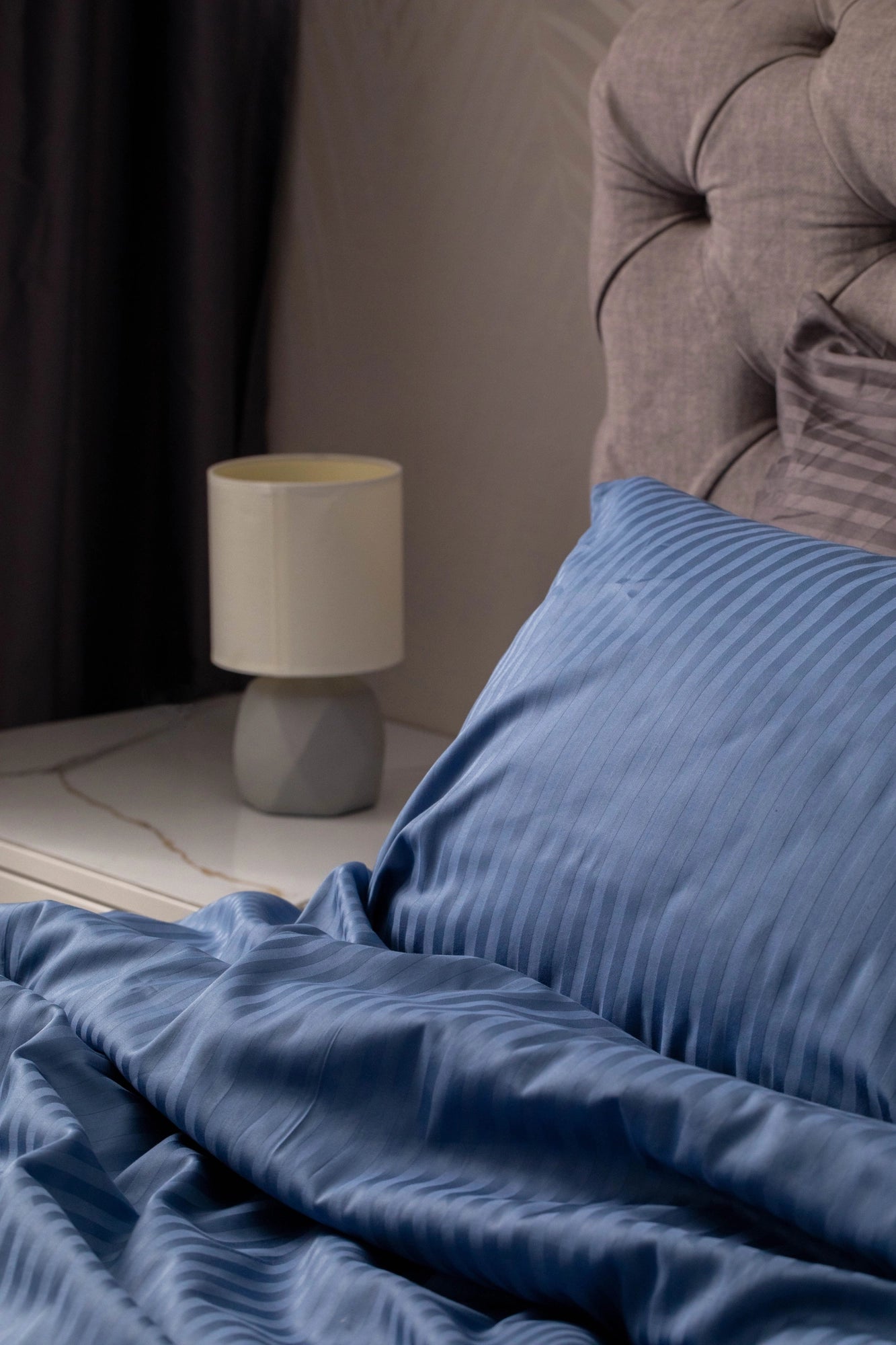 Supreme Rest custom-made ocean blue pillowcase and duvet set in soft sateen weave, styled beside a modern nightstand and upholstered headboard