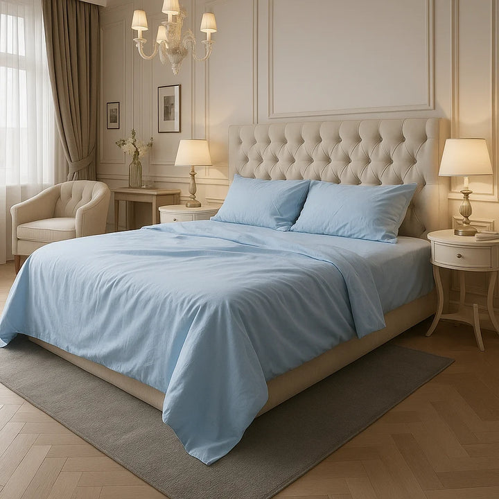 Elegant bedroom with soft sky-blue bedding on a tufted cream headboard bed, styled with classic nightstands, gold lamps, and natural light filtering through sheer curtains