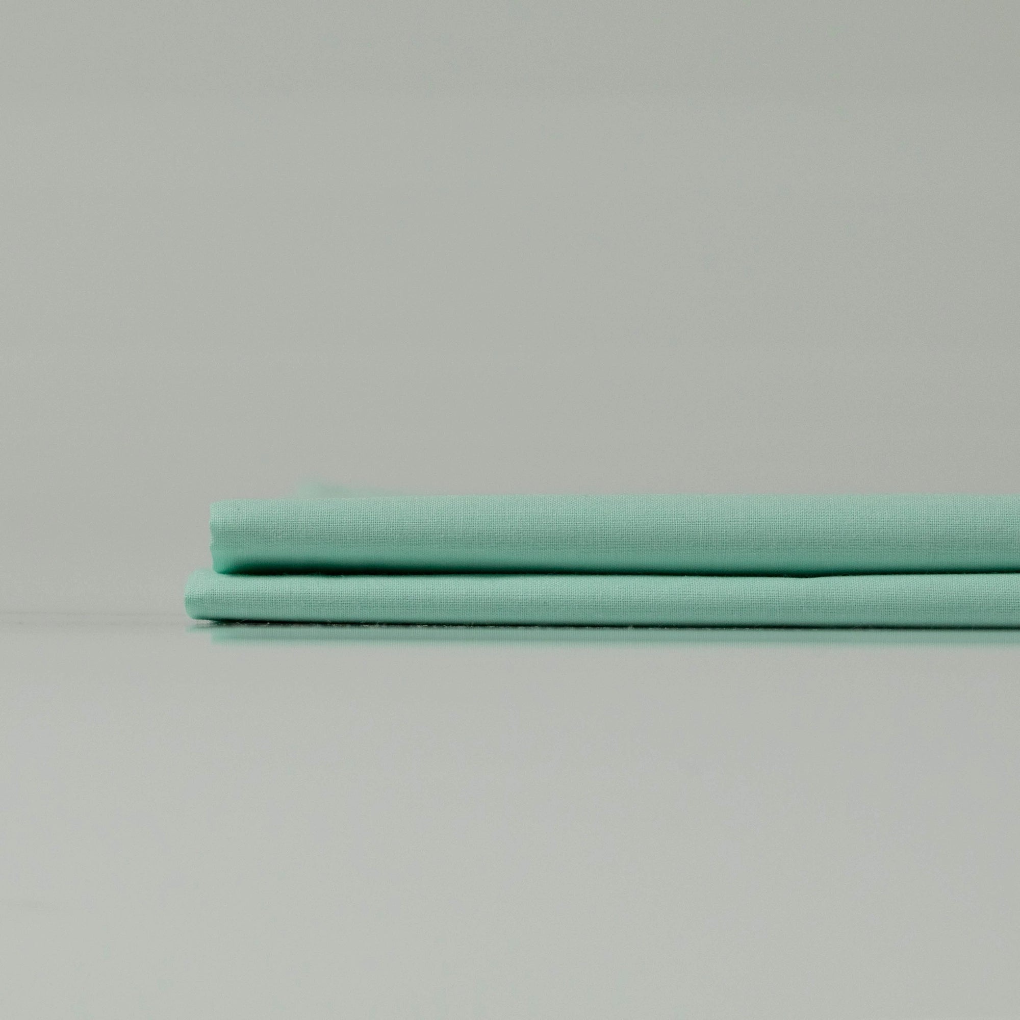 Neatly folded Supreme Rest Glacial Waters ranforce sheets stacked on a flat surface, showcasing their smooth texture.
