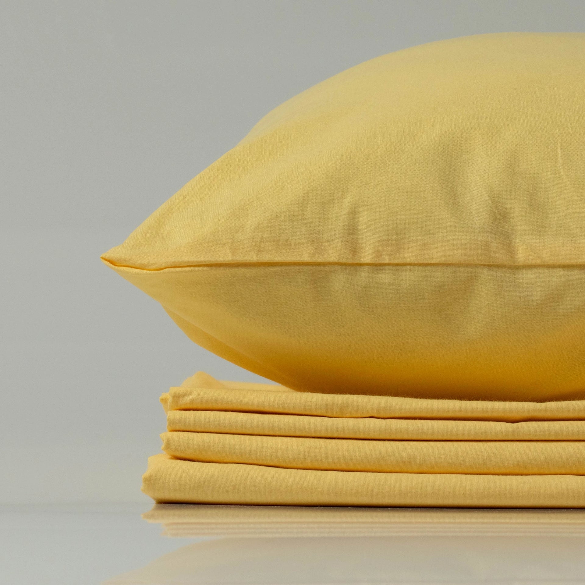 Soft yellow ranforce pillowcase from Supreme Rest resting on a neatly stacked bedding set.