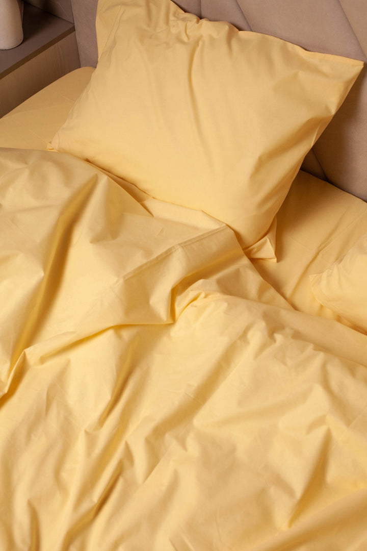 Supreme Rest Lemon Sunbeam ranforce bedding set on a bed, featuring a soft yellow pillowcase and duvet cover with natural folds.