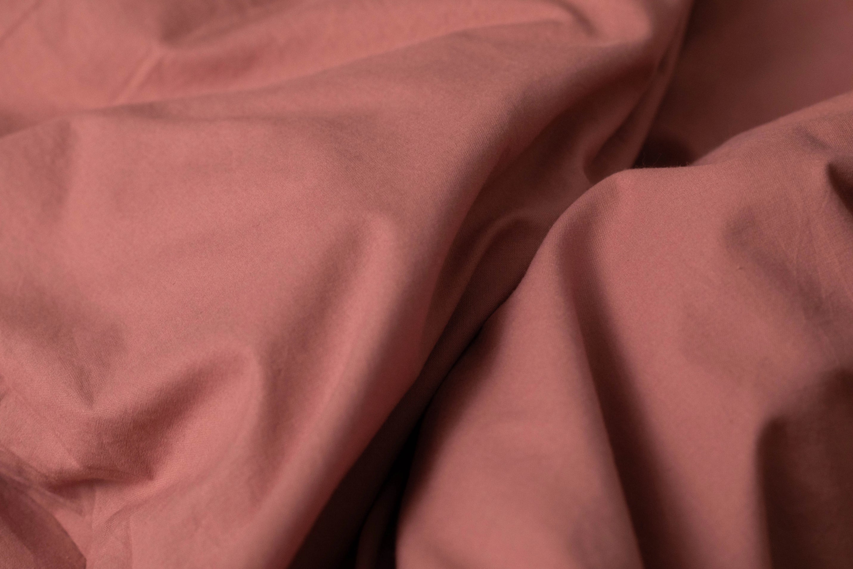 Detail of rumpled rose-hued cotton fabric from Supreme Rest, highlighting its ultra-smooth drape, premium weave quality, and rich earthy pigment ideal for luxury bedding collections