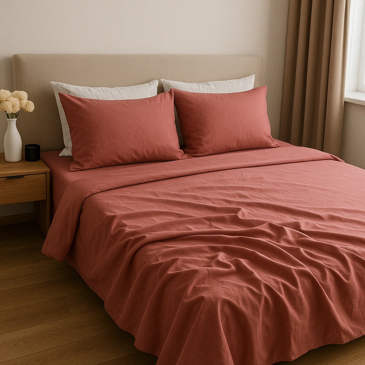 oftly rumpled clay-red bed sheets in a sunlit bedroom, styled with off-white pillows and natural wood accents—Supreme Rest’s breathable cotton bedding for effortless comfort and organic style.