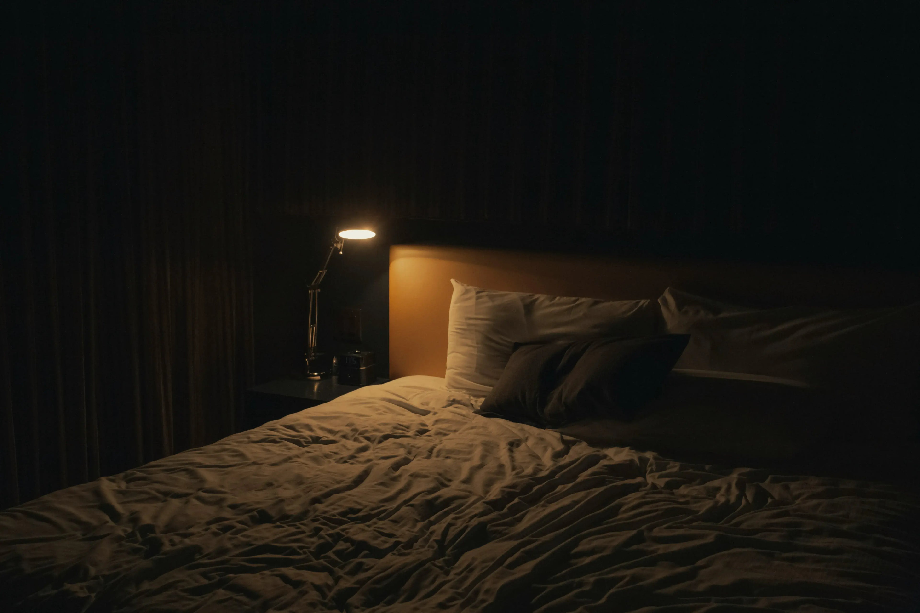 Minimalist bedroom at night with custom bedding, bedside lamp glow, and cozy layered pillows for relaxation.