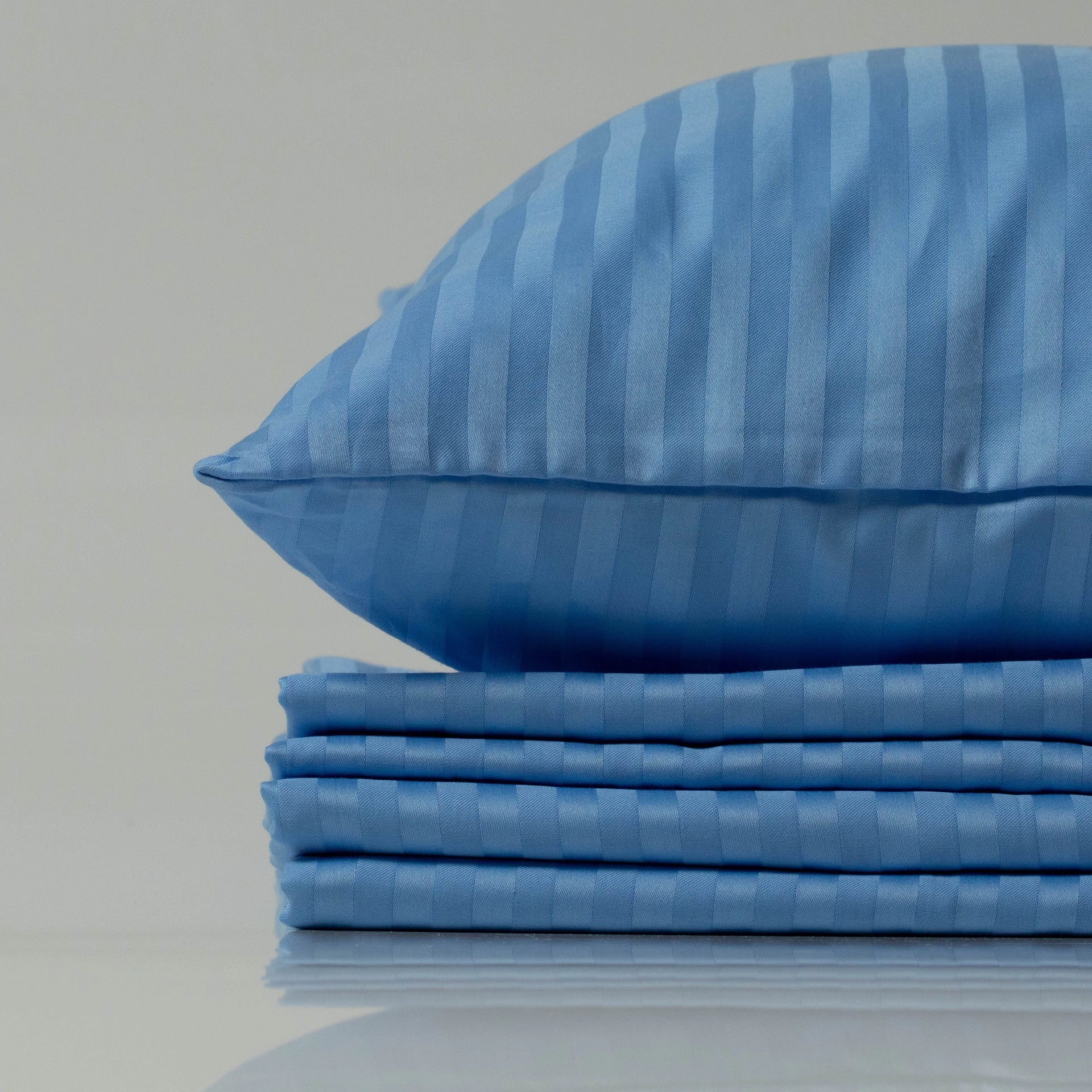 Supreme Rest Celestial Blue striped sateen pillowcase on a neatly stacked bedding set.