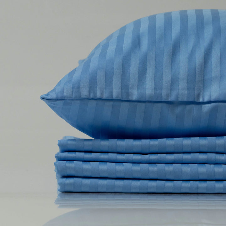 Supreme Rest Celestial Blue striped sateen pillowcase on a neatly stacked bedding set.
