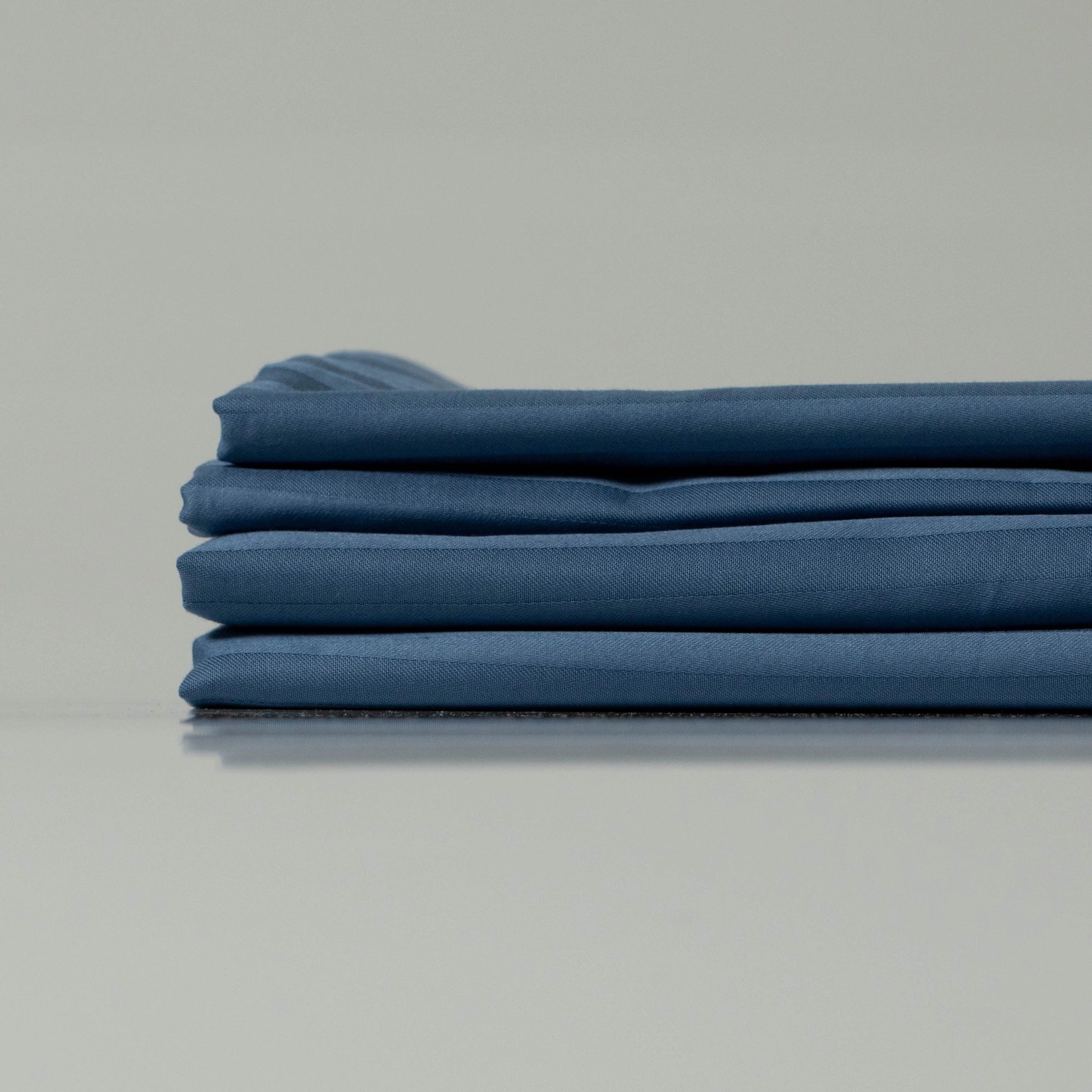 Stack of deep navy blue striped bedsheets, neatly folded to showcase their smooth texture and custom-tailored finish