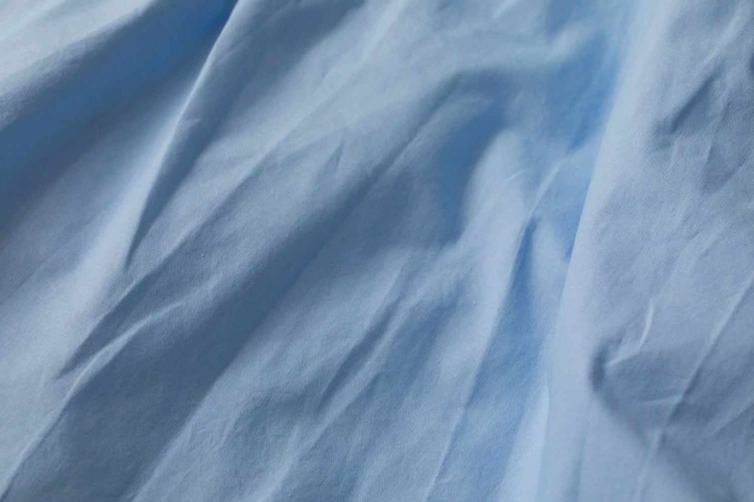 Premium organic cotton sheets in a serene sky blue—elegantly rumpled to reveal their ultra-soft, breathable texture and sustainable craftsmanship