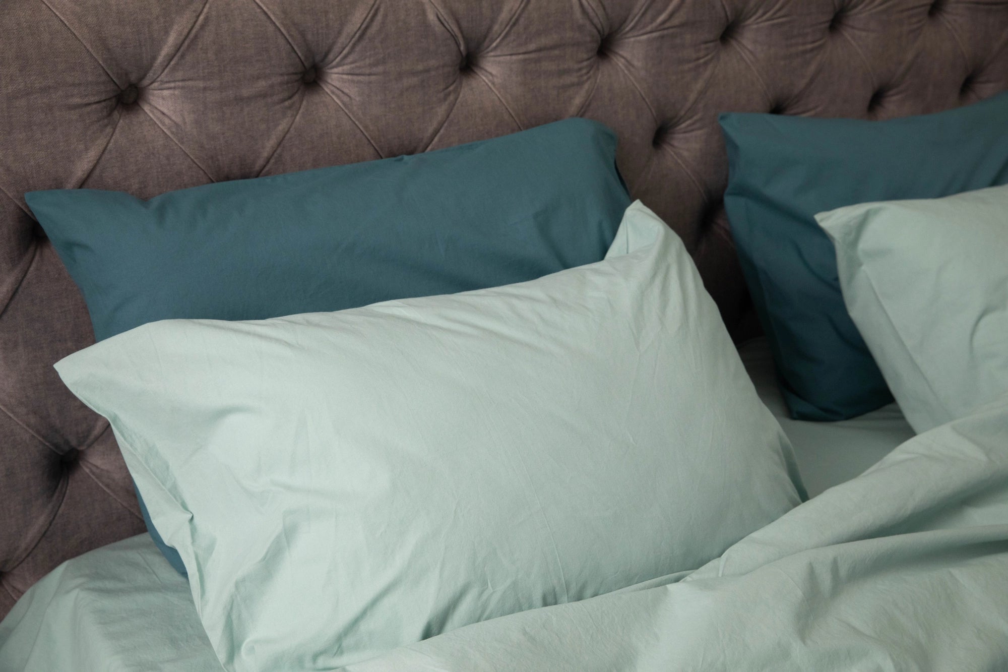 Supreme Rest bed set featuring custom made pillowcases in sage and deep teal, styled against a tufted headboard for a refined, eco-friendly bedroom look