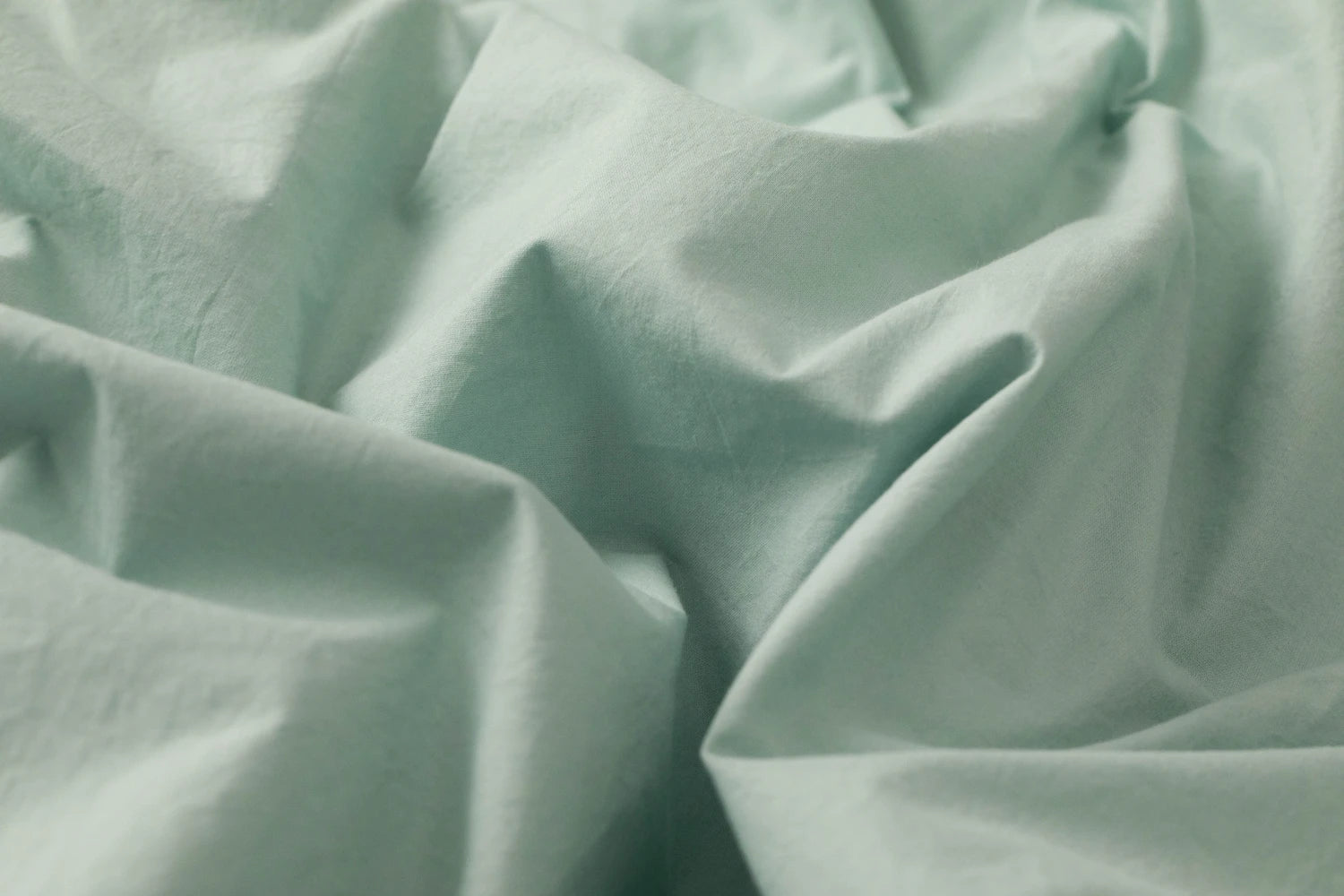 Wrinkled seafoam green cotton sheets in soft natural light, highlighting their breathable, lightweight texture