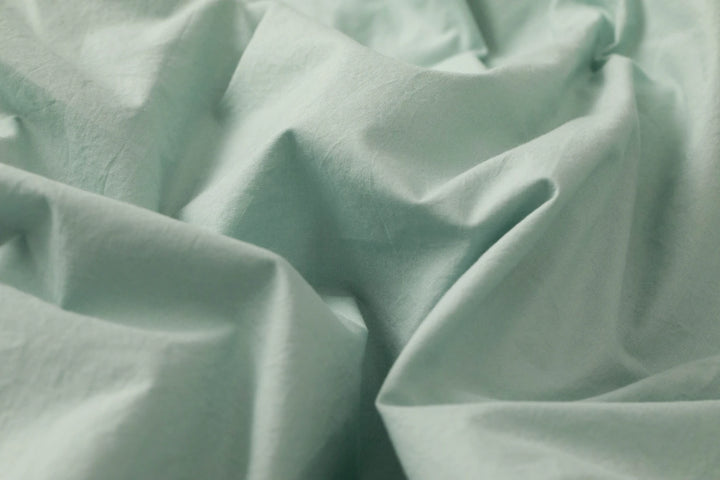 Wrinkled seafoam green cotton sheets in soft natural light, highlighting their breathable, lightweight texture