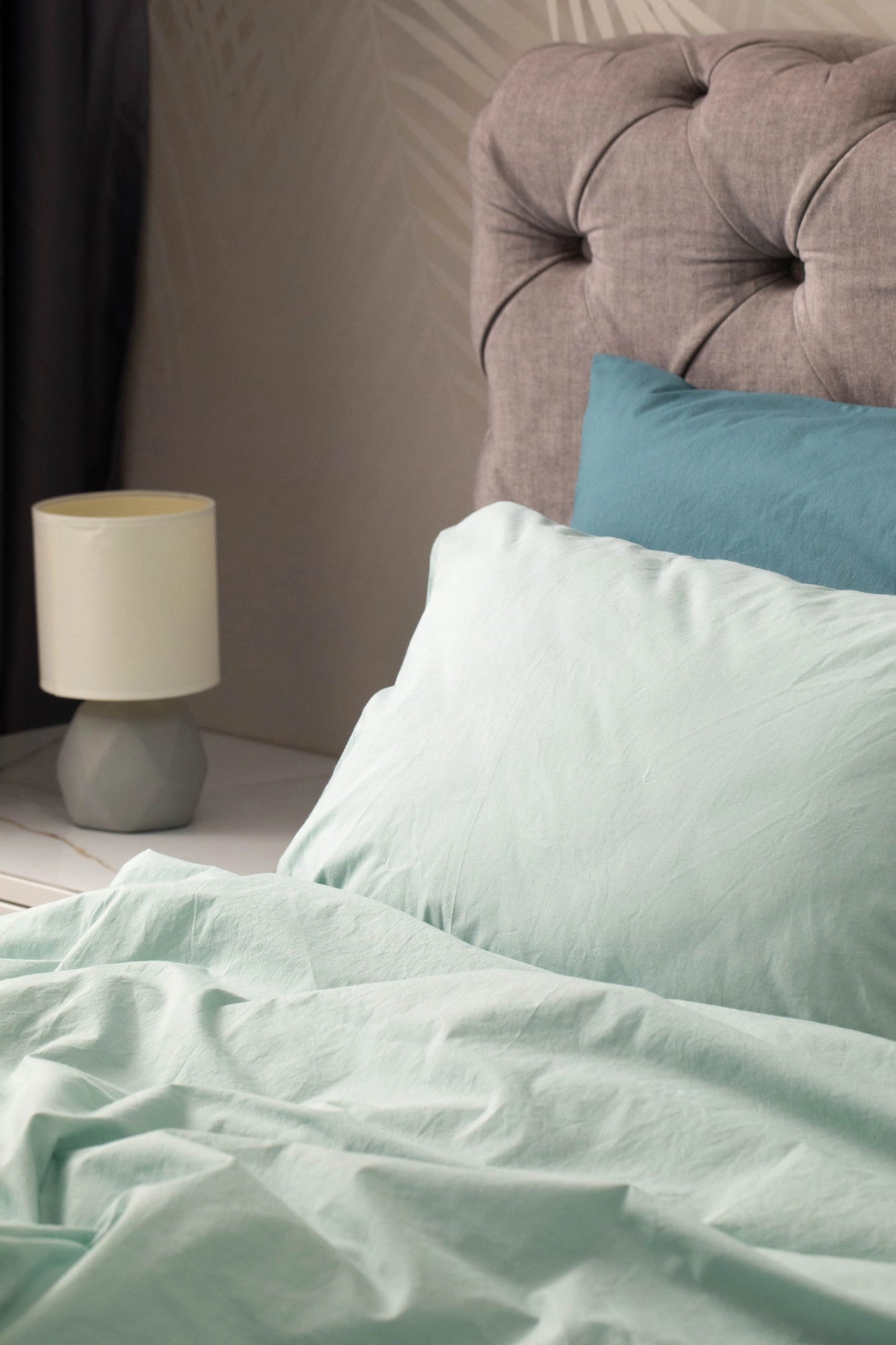 Supreme Rest’s eco-friendly bedding in sage green, styled with a tufted headboard and bedside lamp, showcasing soft textures and custom-made elegance