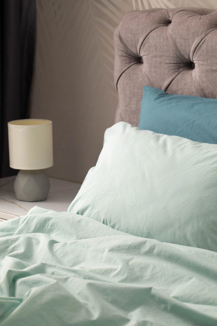 Supreme Rest’s eco-friendly bedding in sage green, styled with a tufted headboard and bedside lamp, showcasing soft textures and custom-made elegance