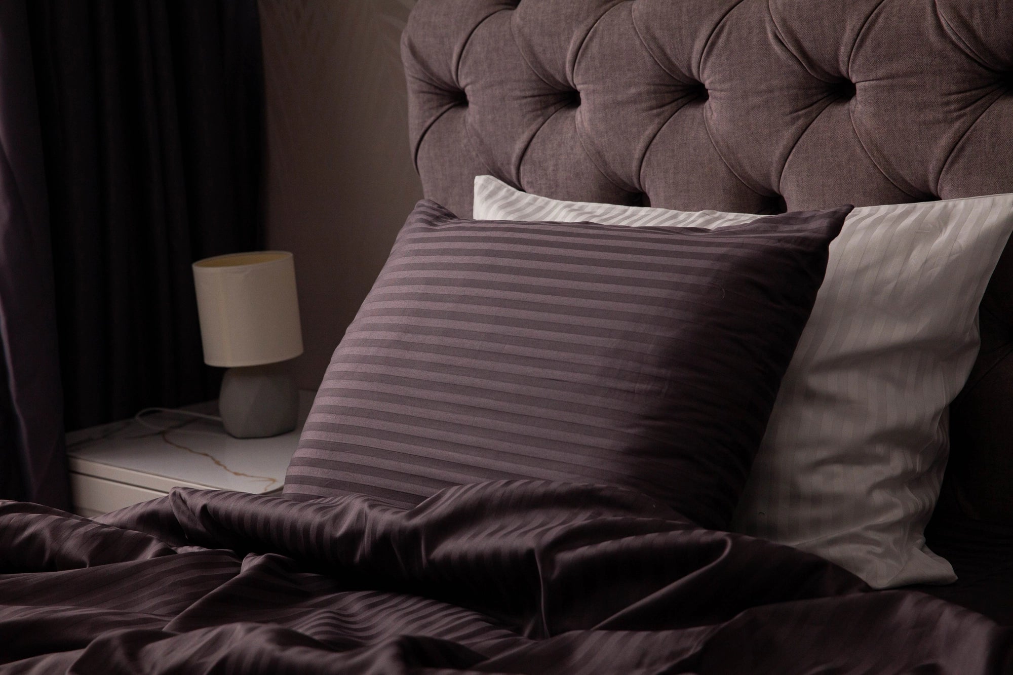 Supreme Rest custom-made striped pillowcases in rich plum and ivory tones, layered for a luxurious, eco-friendly bedding presentation against a tufted headboard