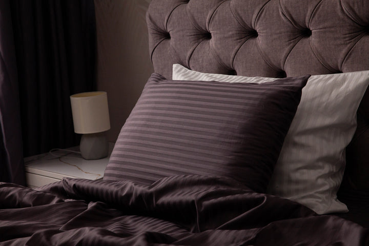 Supreme Rest custom-made striped pillowcases in rich plum and ivory tones, layered for a luxurious, eco-friendly bedding presentation against a tufted headboard