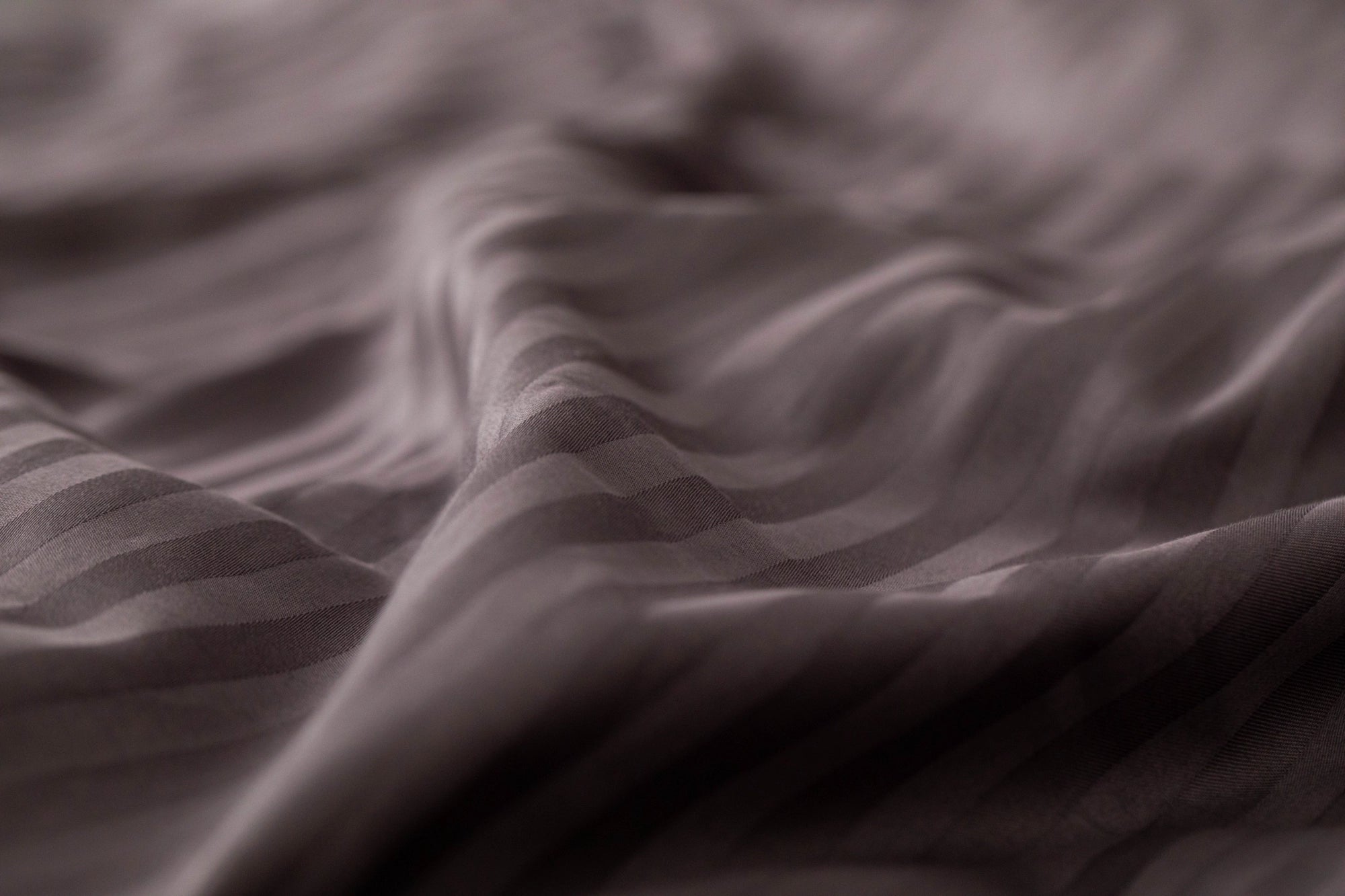 Detail of Supreme Rest's custom made, eco-friendly bedding showing soft striped waves in deep plum, highlighting the silky craftsmanship and texture