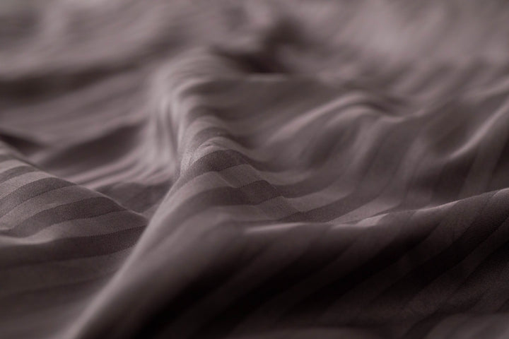 Detail of Supreme Rest's custom made, eco-friendly bedding showing soft striped waves in deep plum, highlighting the silky craftsmanship and texture