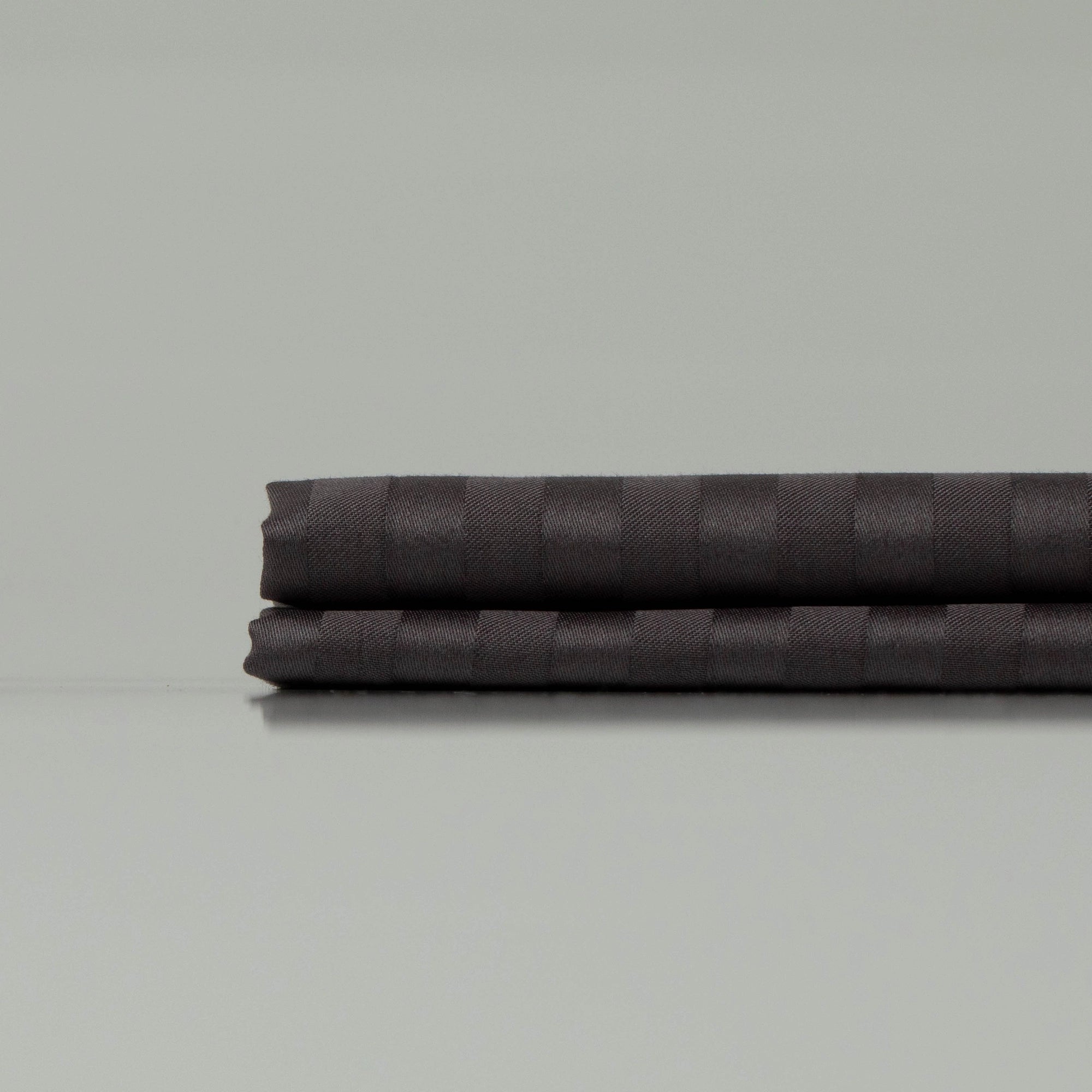 Neatly folded dark striped sateen pillowcases from Supreme Rest, showcasing eco-friendly luxury and refined craftsmanship