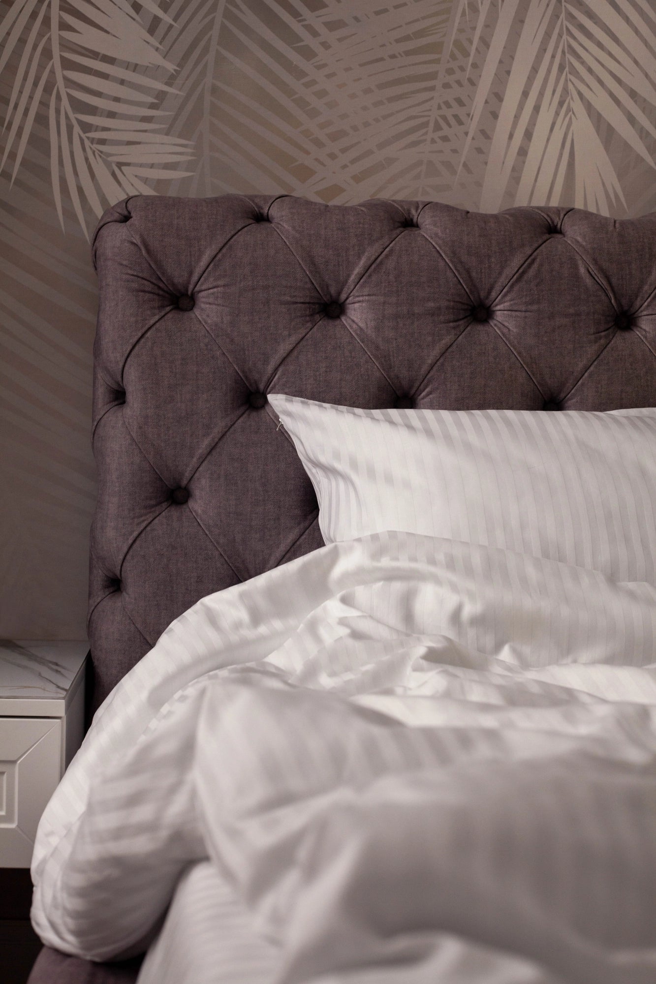 Detail of artisan tufted headboard paired with custom white striped linens, capturing Supreme Rest’s blend of eco-conscious comfort and refined design