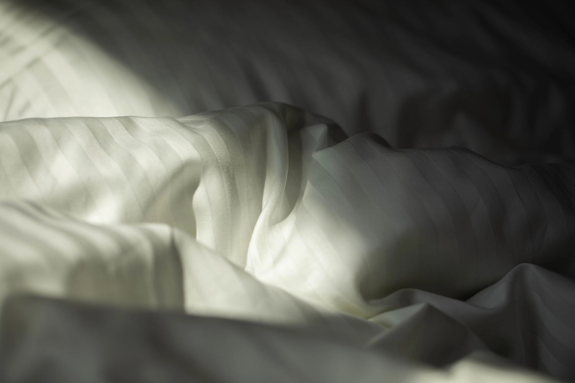 Close-up of silky-smooth Supreme Rest Ivory Dune sateen fabric, highlighting its delicate sheen.