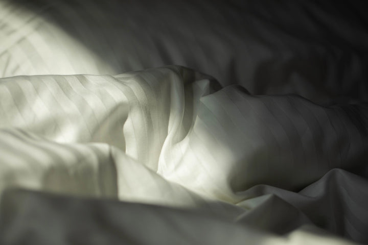Close-up of silky-smooth Supreme Rest Ivory Dune sateen fabric, highlighting its delicate sheen.