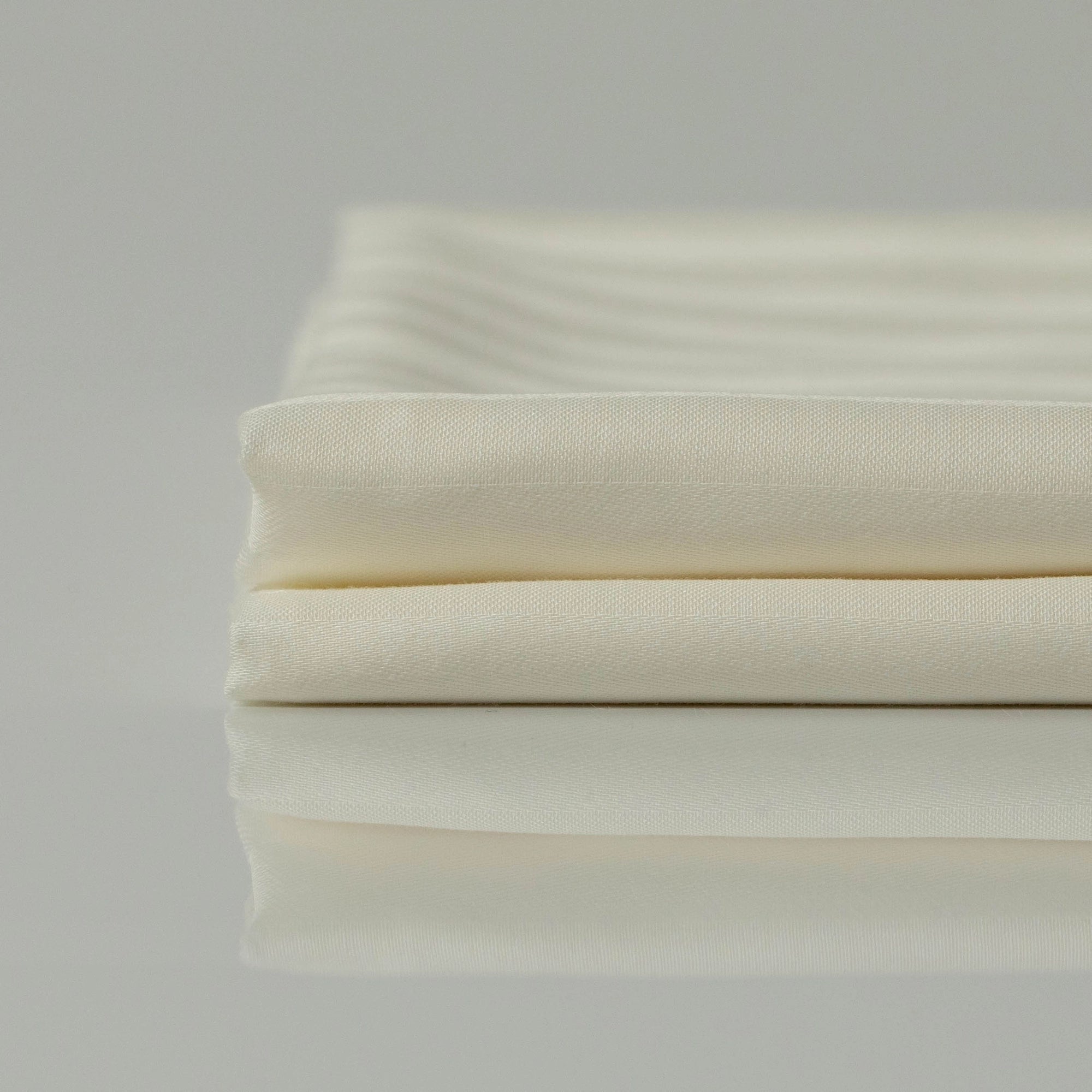 Stacked Supreme Rest Ivory Dune sateen sheets, emphasizing their silky texture and durability.