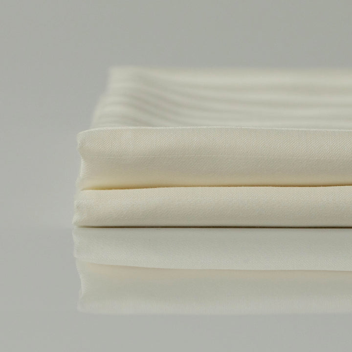 Stacked Supreme Rest Ivory Dune sateen sheets, emphasizing their silky texture and durability.