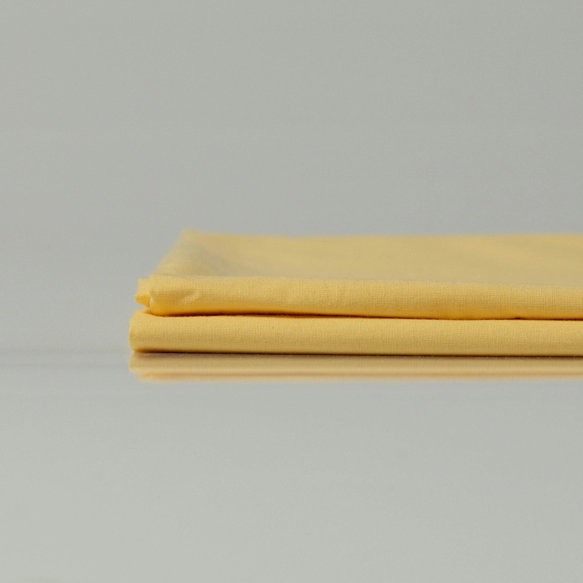 Neatly folded Supreme Rest Lemon Sunbeam ranforce sheets in soft yellow, showcasing smooth texture and breathable cotton fabric.
