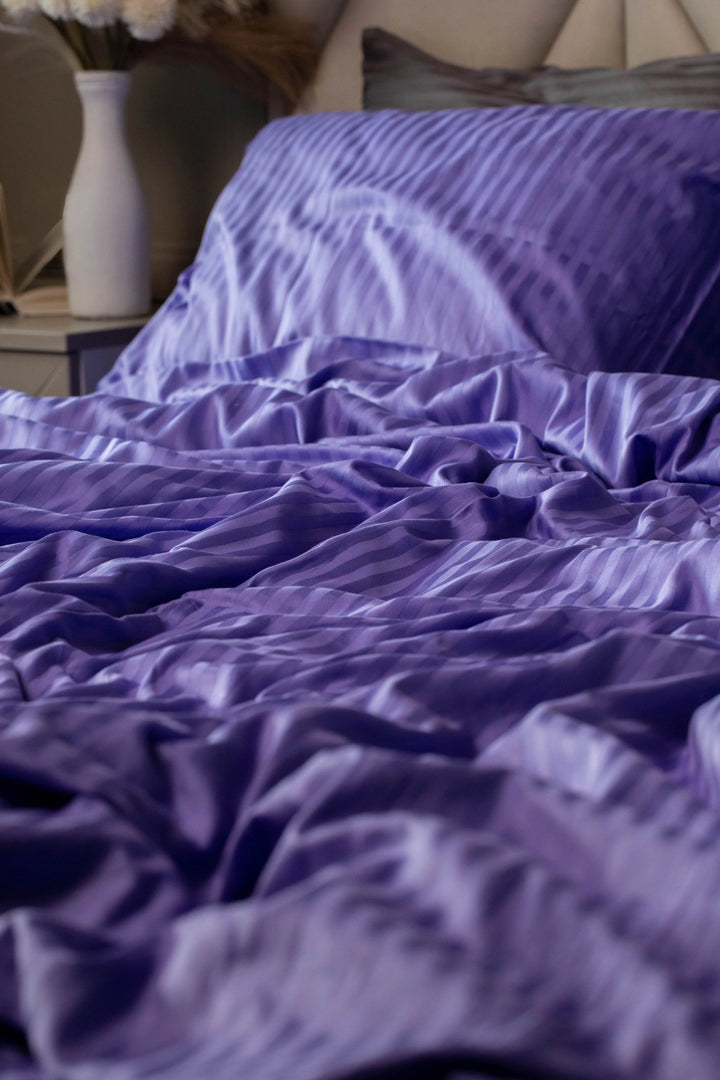 Luxurious Supreme Rest Patagonian Lupine striped sateen duvet cover in deep purple, elegantly draped over a bed.