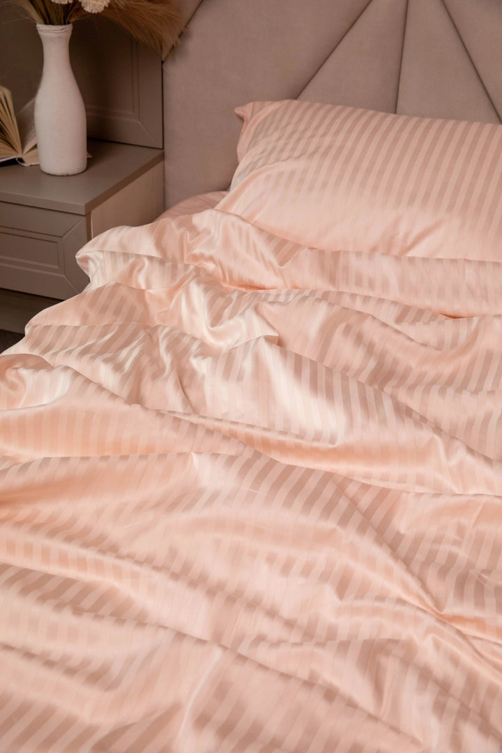 Supreme Rest blush-toned bedding set with subtle satin stripes, styled in a serene bedroom for an inviting, eco-friendly luxury look