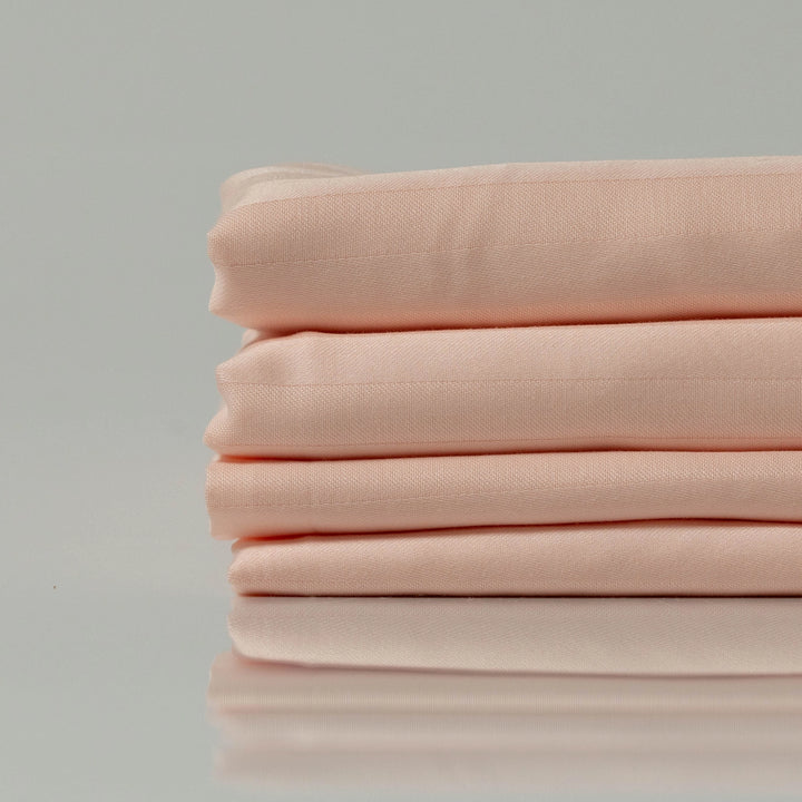 Neatly stacked peach-toned cotton fabric folded on a glossy surface with soft lighting