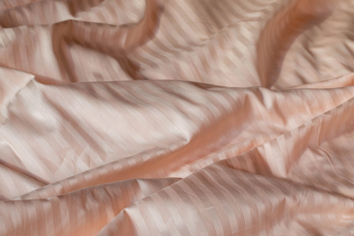 Close-up of Supreme Rest bedding in a soft peach hue with a striped sateen finish, showcasing the eco-friendly, custom-made craftsmanship
