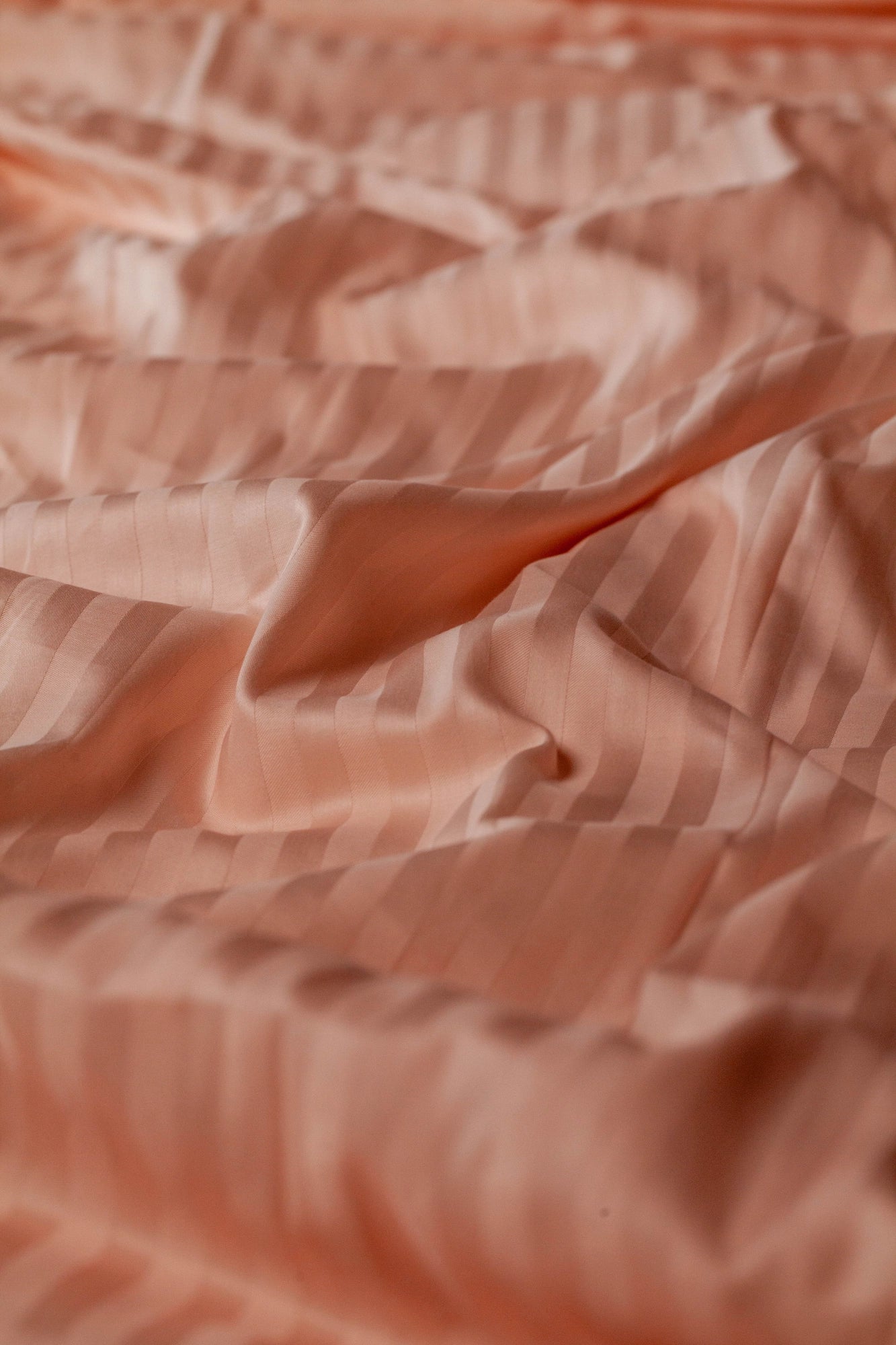 Detail shot of blush peach Supreme Rest bedding in subtle sateen stripes, highlighting the eco-friendly weave and smooth handcrafted texture