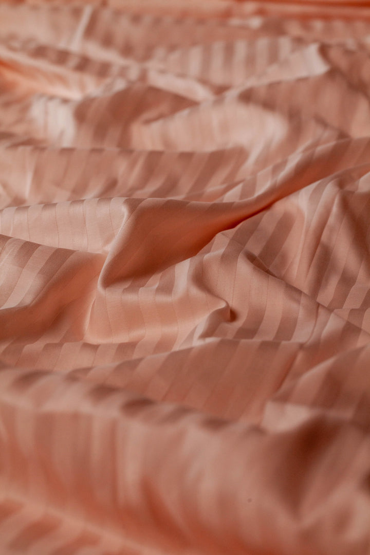 Detail shot of blush peach Supreme Rest bedding in subtle sateen stripes, highlighting the eco-friendly weave and smooth handcrafted texture