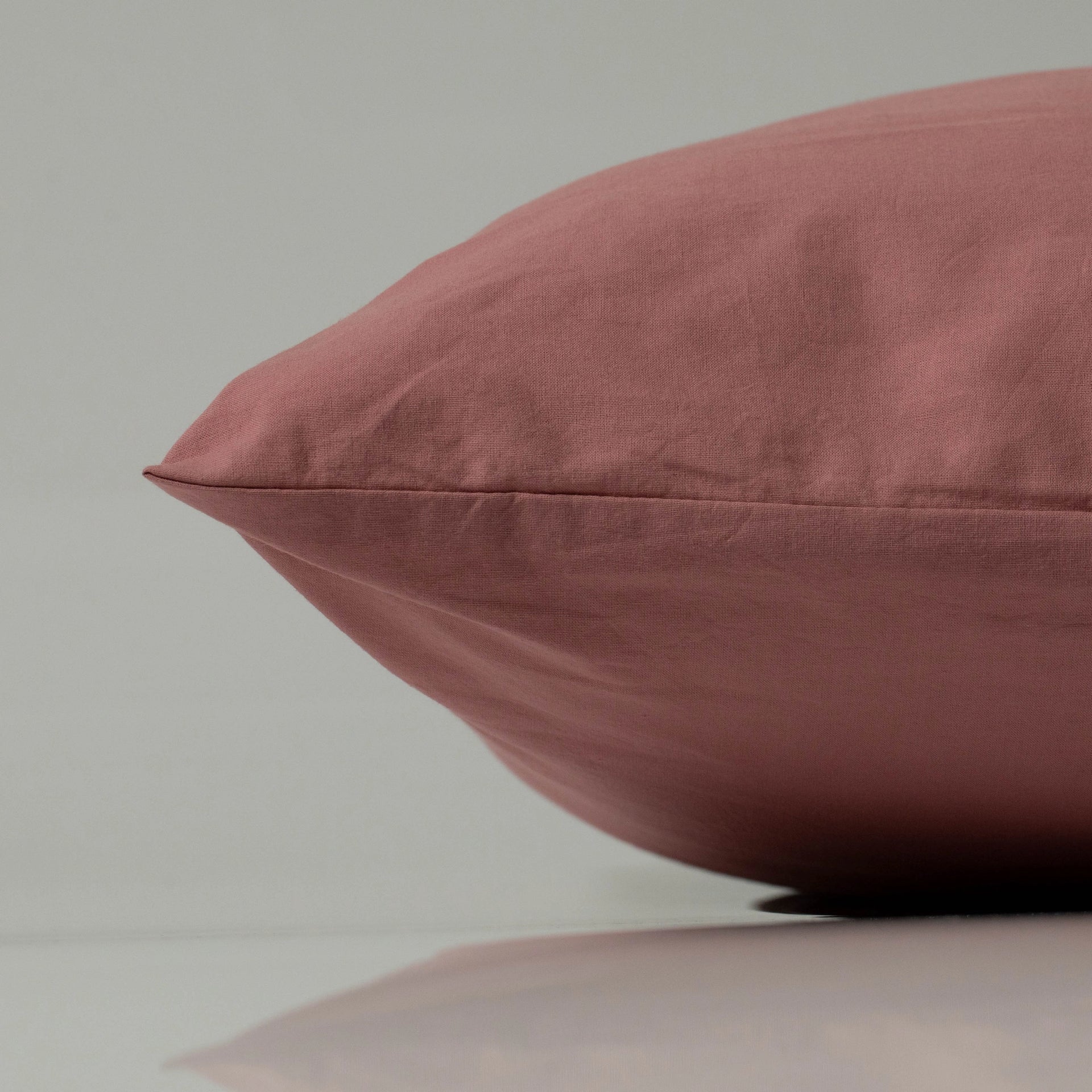Terracotta pillow with a smooth cotton surface and subtle seam detail, resting on a reflective surface for a clean, modern presentation.