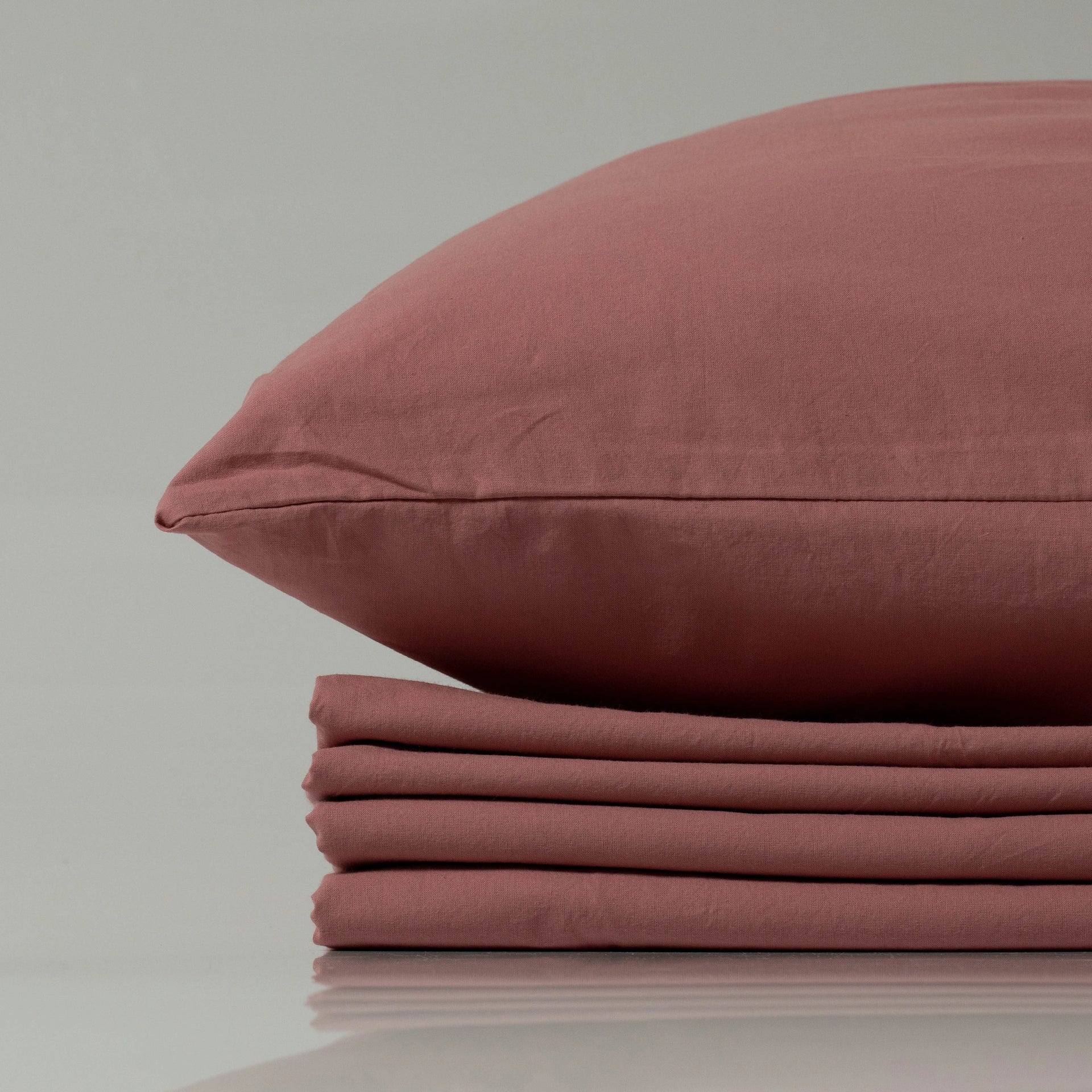 Stacked terracotta pillow and sheets in a matte finish, radiating an earthy, understated elegance with tailored edges and a soft, lived-in texture