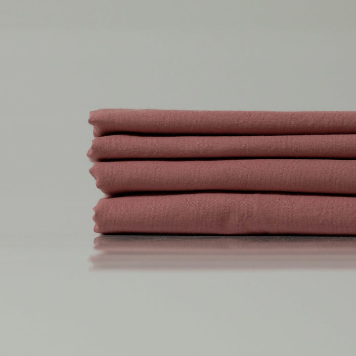 A refined stack of dusky rose-hued cotton bedding, showcasing a soft, lived-in texture and a serene, minimalist composition