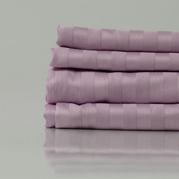 Stack of lavender-striped bed linens, neatly folded to showcase their silky texture and refined tailoring for a serene bedroom aesthetic