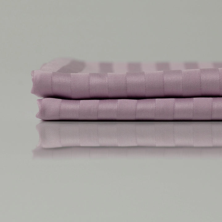 Two lavender-striped flat sheets folded with crisp precision, reflecting a soft sheen that hints at their silky, breathable weave