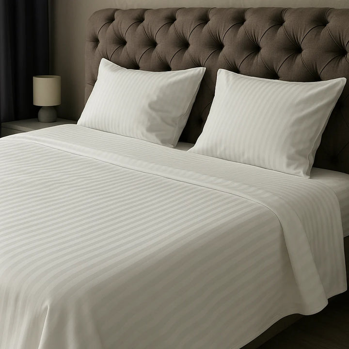 Pure Bliss luxury white bedding with tonal sateen stripes, custom hand-crafted and styled on a tufted headboard bed in a softly lit, elegant bedroom