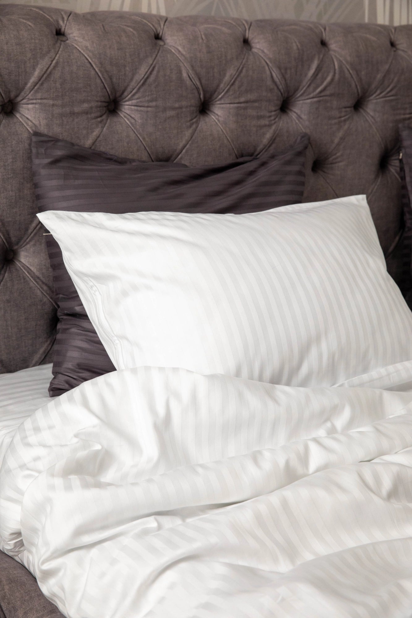 Close-up of Supreme Rest’s crafted white striped pillow and duvet set, elegantly layered over dark accent cushions for a custom made and eco-friendly bedroom aesthetic