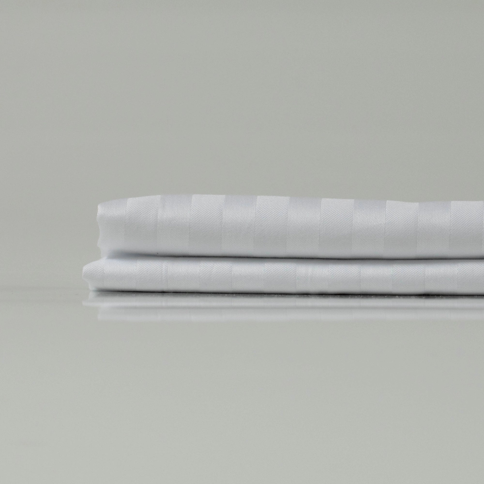 Two crisply folded white sheets with tonal stripes, exuding a minimalist sophistication tailored for refined, modern bedrooms