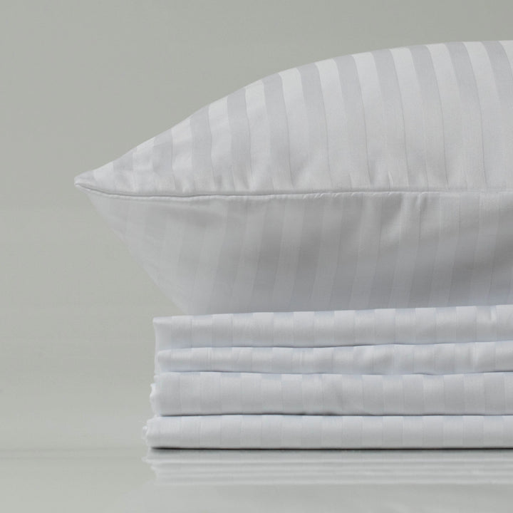 Stack of crisp, folded white sateen-striped bed sheets topped with a matching pillow, conveying a clean, polished hotel-style luxury