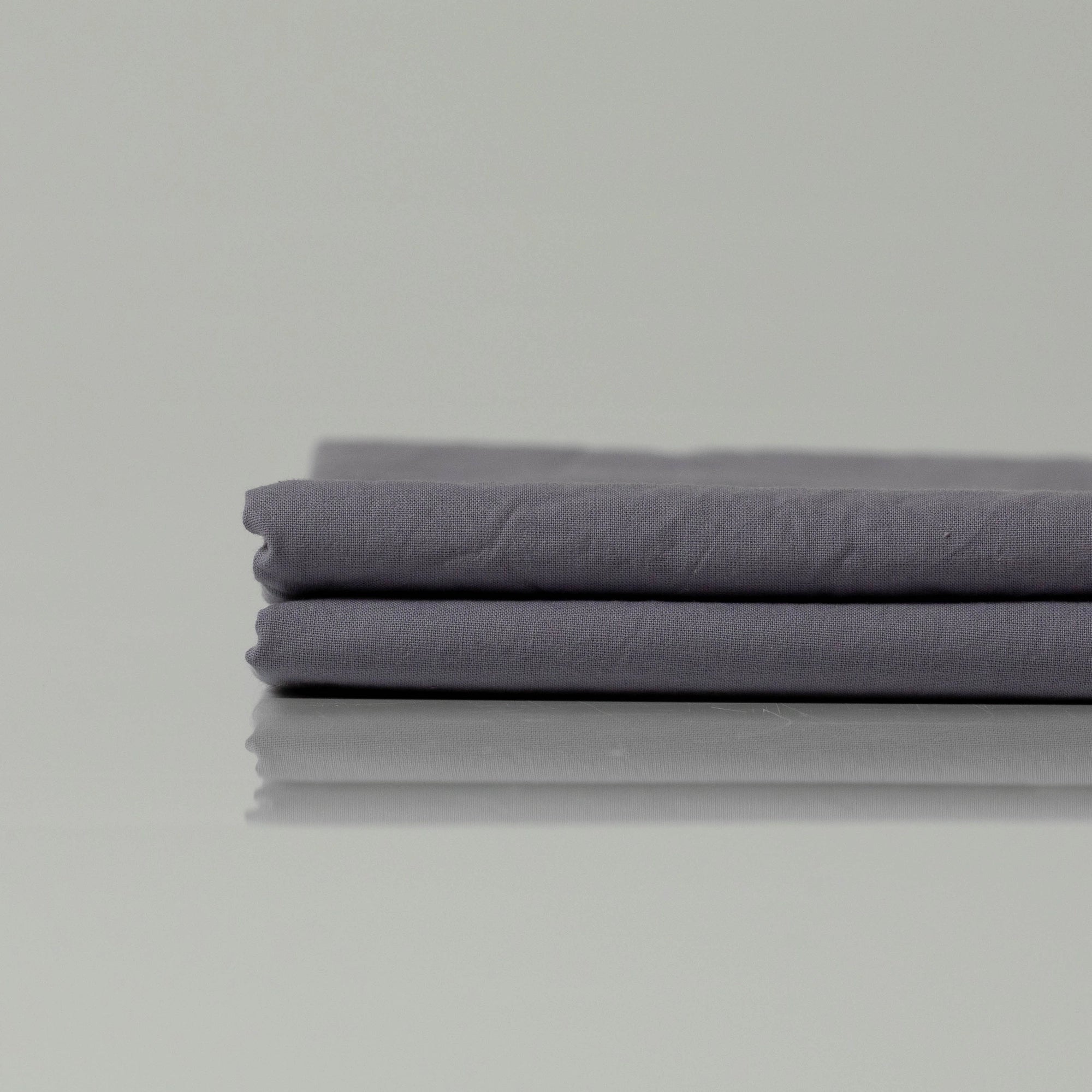 Folded bed sheets in a muted graphite tone, crafted from high-quality cotton with a smooth, understated texture